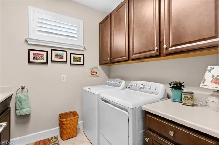 Dedicated laundry space featuring a window with white louvered blinds, ample upper cabinetry, and a countertop with lower cabinetry