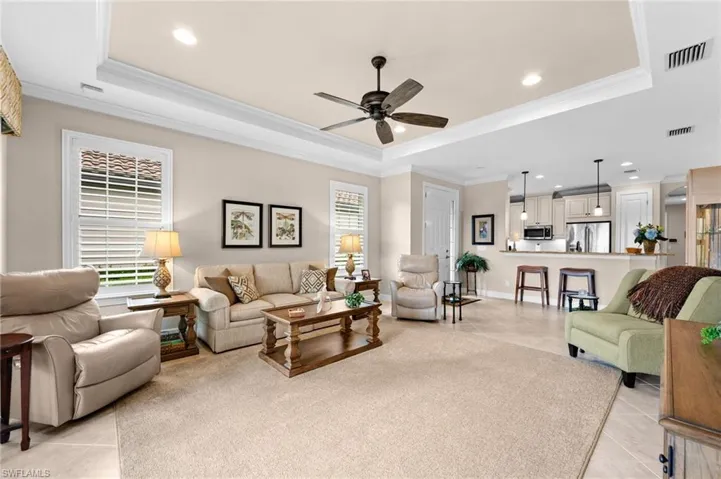 Spacious living area featuring tray ceilings with crown molding, recessed lighting, and a ceiling fan