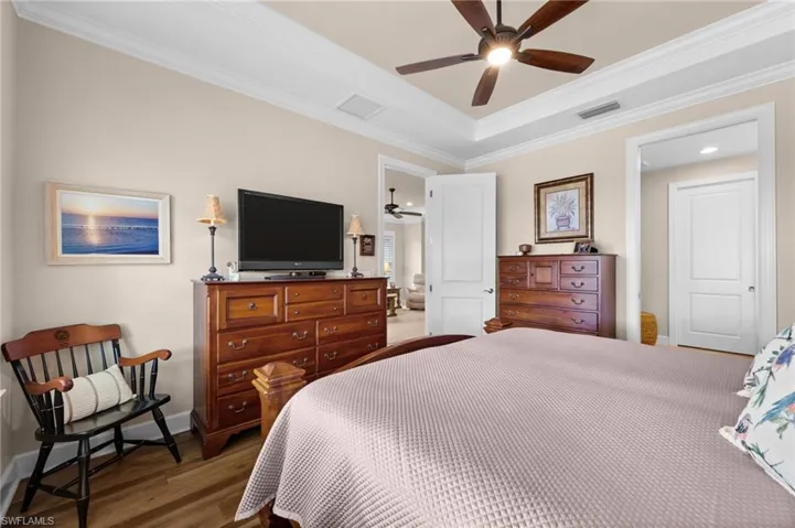 Bedroom featuring a tray ceiling with a ceiling fan, crown molding, and wood-finish flooring