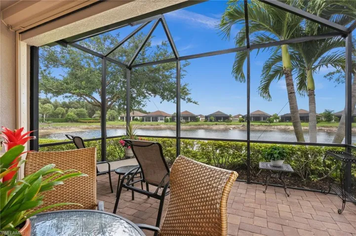 Screened lanai featuring paver flooring, a tranquil waterfront, lush landscaping, and mature palm trees