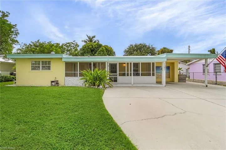 Back of property featuring a sunroom, concrete driveway, stucco siding, and a carport