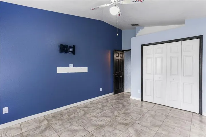 Unfurnished bedroom with ceiling fan, a closet, vaulted ceiling, and light tile patterned flooring