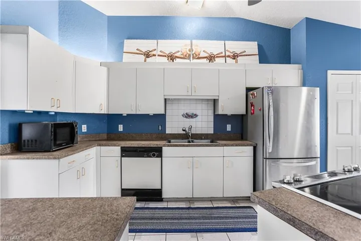 Kitchen featuring backsplash, stainless steel refrigerator, vaulted ceiling, white dishwasher, and sink