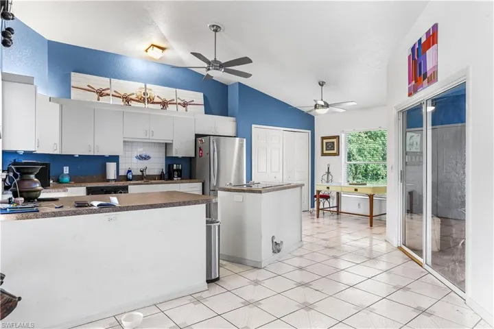Kitchen featuring a center island, vaulted ceiling, stainless steel refrigerator, ceiling fan, and white cabinets