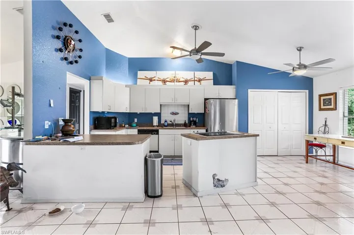 Kitchen with a center island, white dishwasher, stainless steel refrigerator, ceiling fan, and white cabinetry