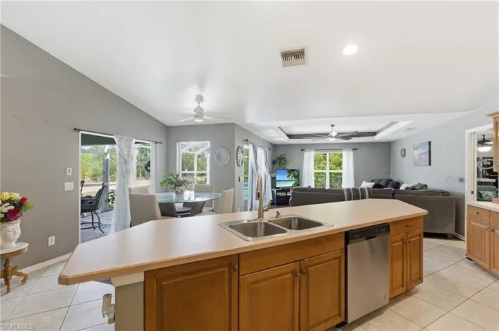 Kitchen featuring open floor plan, light countertops, stainless steel dishwasher, a kitchen island with sink, and a tray ceiling