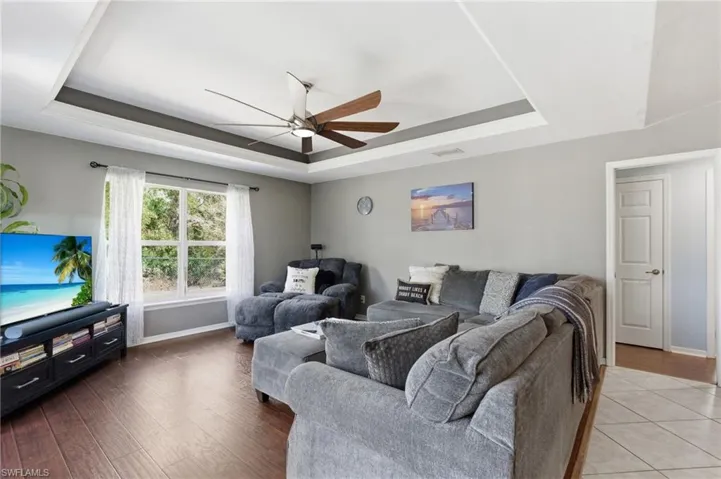 Living area with ceiling fan, a tray ceiling, and wood finished floors