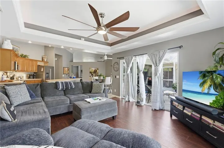 Living area featuring a raised ceiling, dark wood-type flooring, ceiling fan, and crown molding