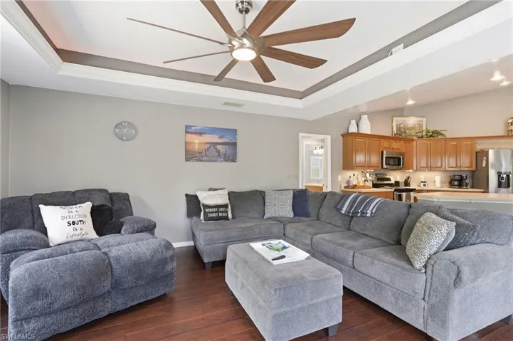 Living area featuring crown molding, a tray ceiling, dark wood finished floors, and ceiling fan
