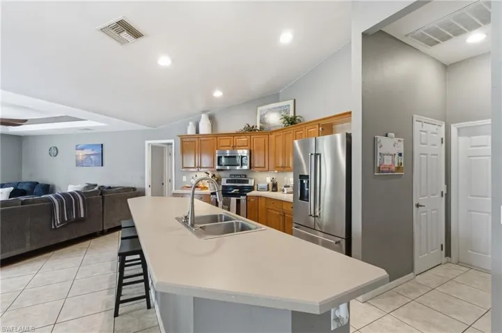 Kitchen with stainless steel appliances, wood finish cabinetry, a kitchen breakfast bar, a kitchen island with sink, and vaulted ceiling