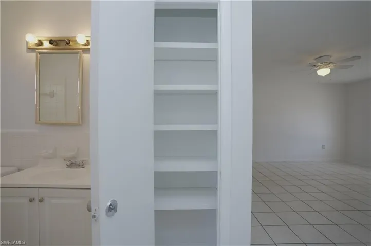 Bathroom vanity with a mirror and overhead lighting, alongside built-in shelving, and a room with tiled flooring and a ceiling fan