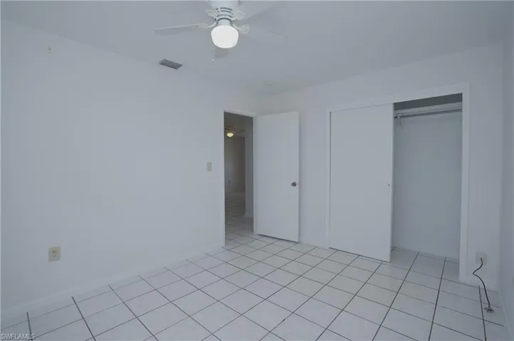 This room features white tile flooring, a ceiling fan with integrated lighting, and a closet with sliding doors