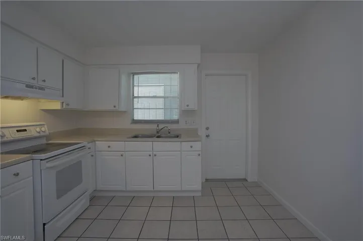 The kitchen features white cabinetry, a double basin sink, and a white electric range