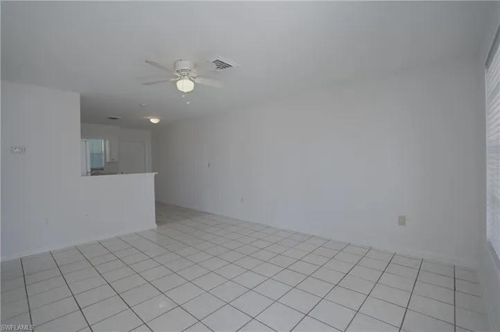 This living area features tile flooring, a ceiling fan with integrated lighting, and a window with blinds