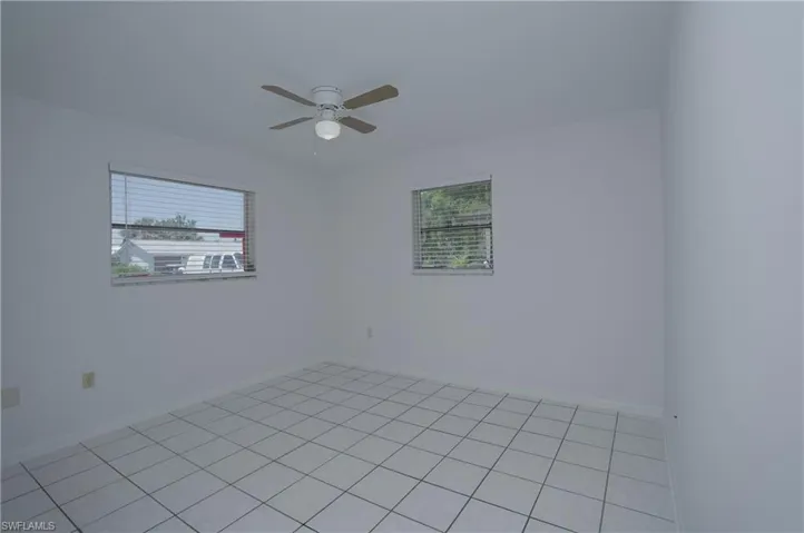 Room featuring white tile flooring, windows with blinds, and a ceiling fan with light fixture
