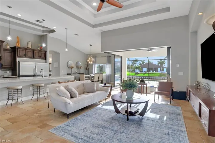 Living area featuring a raised ceiling, a high ceiling, a ceiling fan, recessed lighting, and a chandelier