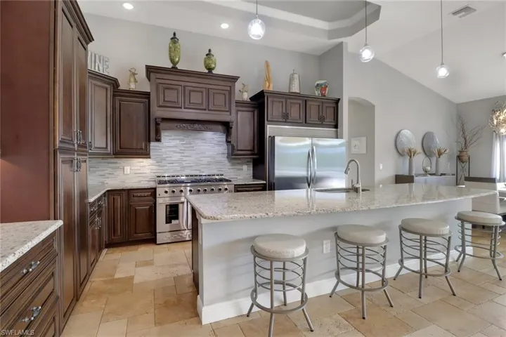 Kitchen featuring dark brown cabinets, a kitchen breakfast bar, stainless steel appliances, hanging light fixtures, and vaulted ceiling