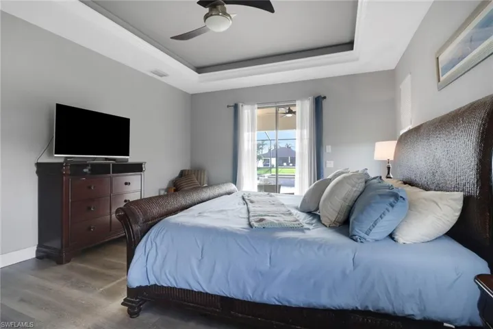 Bedroom featuring a tray ceiling, wood finished floors, a ceiling fan, and access to exterior