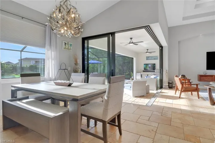 Dining space featuring a sunroom, stone tile flooring, a ceiling fan, a chandelier, and vaulted ceiling