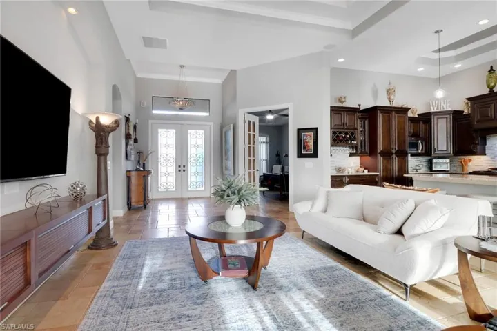 Living room with french doors, a raised ceiling, recessed lighting, a high ceiling, and crown molding