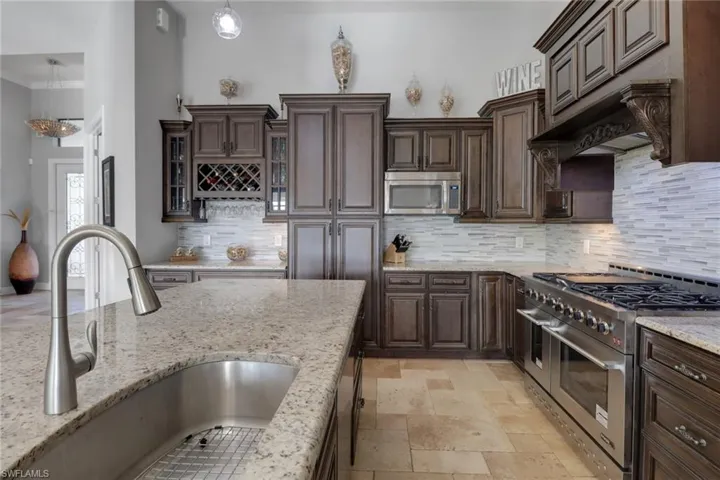 Kitchen with stainless steel appliances, backsplash, dark brown cabinetry, light stone countertops, and pendant lighting
