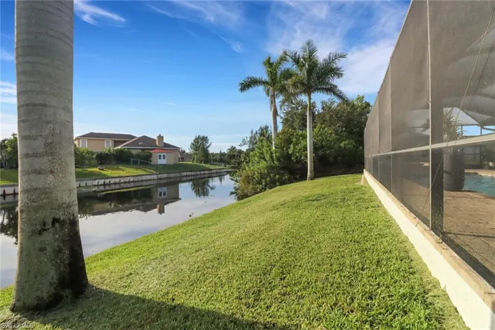 View of grassy yard with a water view, a sunroom, and glass enclosure