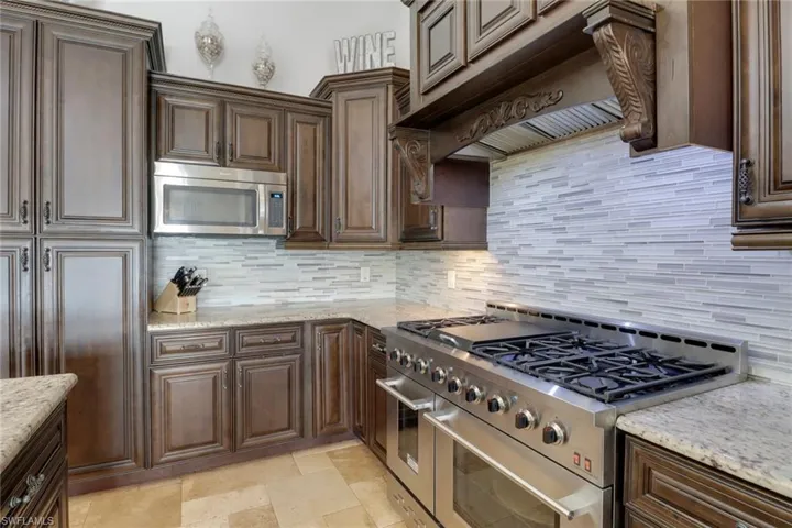 Kitchen featuring appliances with stainless steel finishes, backsplash, dark brown cabinets, and light stone countertops
