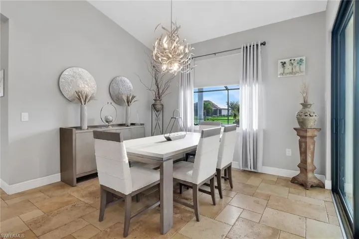 Dining area with stone tile floors, a chandelier, and lofted ceiling
