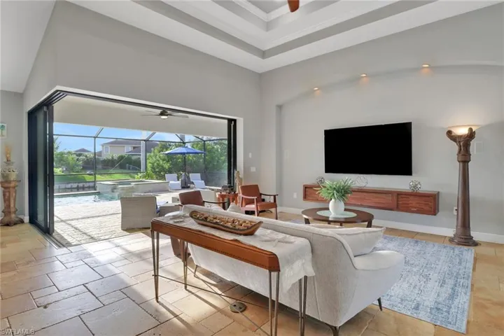 Living area with a sunroom, a towering ceiling, ceiling fan, stone tile floors, and a raised ceiling