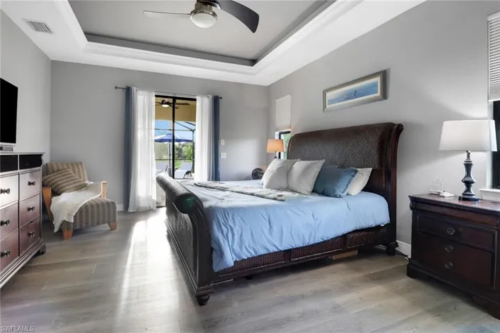 Bedroom with a raised ceiling, access to outside, wood finished floors, and ceiling fan