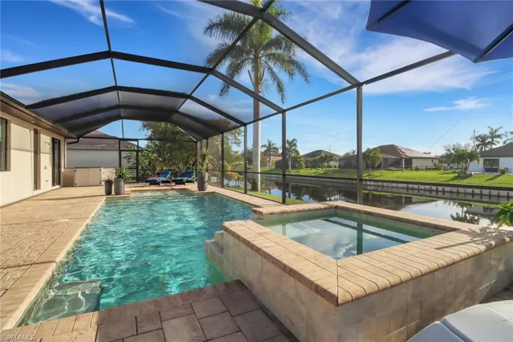 View of pool featuring a sunroom, a water view, a pool with connected hot tub, glass enclosure, and a patio area