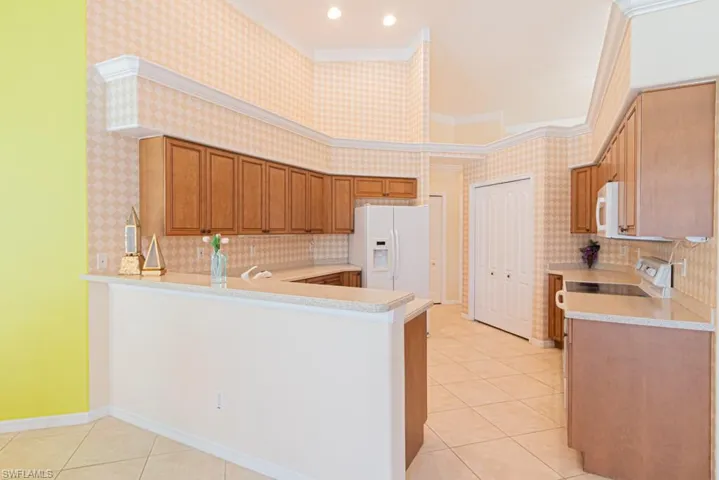 Kitchen featuring sink, light tile patterned floors, white appliances, decorative backsplash, and kitchen peninsula