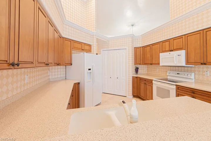 Kitchen featuring crown molding, sink, light stone counters, and white appliances