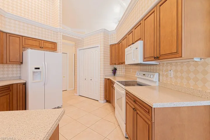 Kitchen with light tile patterned flooring, light stone countertops, ornamental molding, and white appliances