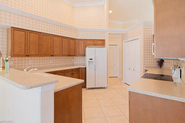 Kitchen with light tile patterned flooring, ornamental molding, white fridge with ice dispenser, range, and kitchen peninsula