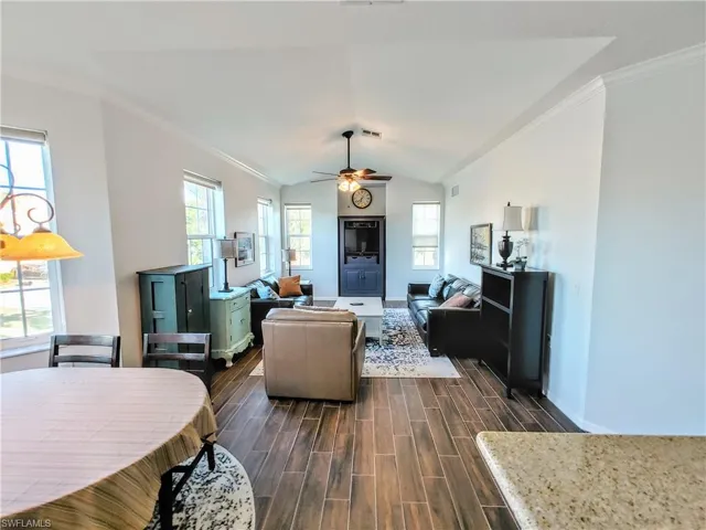 Living room featuring crown molding, dark hardwood / wood-style floors, lofted ceiling, and ceiling fan
