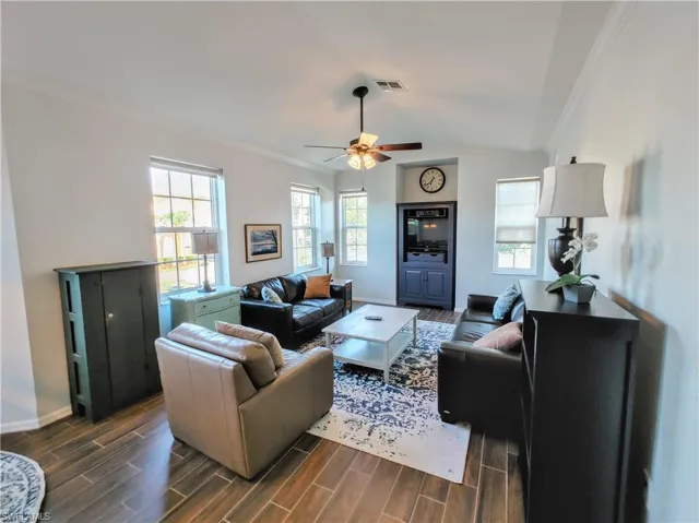 Living room with ceiling fan, dark hardwood / wood-style flooring, lofted ceiling, and ornamental molding