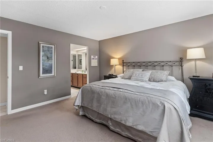 Bedroom with light carpet, ensuite bath, and a textured ceiling