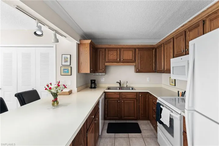 Kitchen featuring a textured ceiling, white appliances, light countertops, a peninsula, and ornamental molding