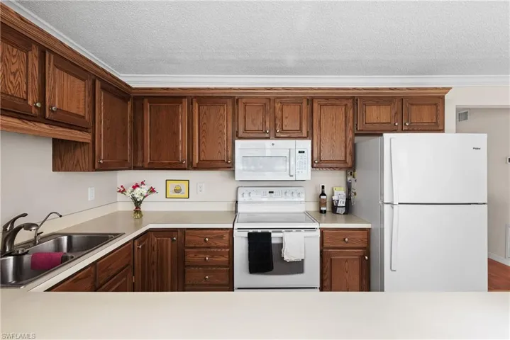 Kitchen with white appliances, light countertops, a textured ceiling, and crown molding