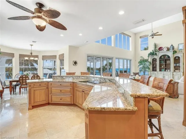 Kitchen with a ceiling fan, a breakfast bar area, light stone countertops, a spacious island, and a high ceiling - Virtually Edited Image