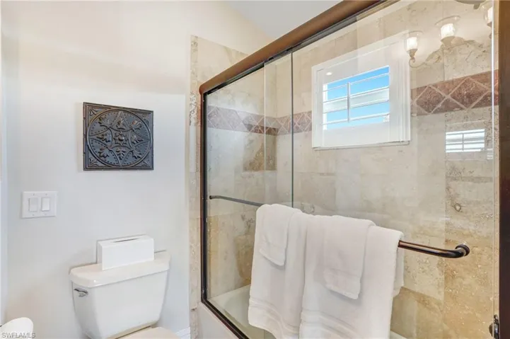 Full bathroom featuring toilet and bath / shower combo with glass door - Virtually Edited Image