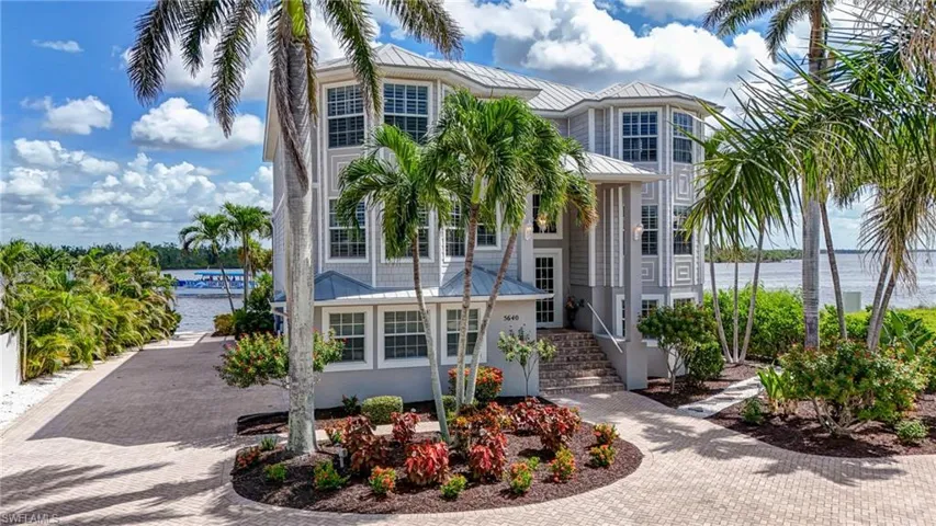 View of front of house featuring a water view, a standing seam roof, curved driveway, and stucco siding - Virtually Edited Image