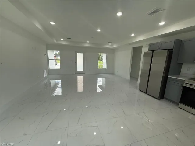 Empty room featuring a tray ceiling, recessed lighting, and light marble finish floors