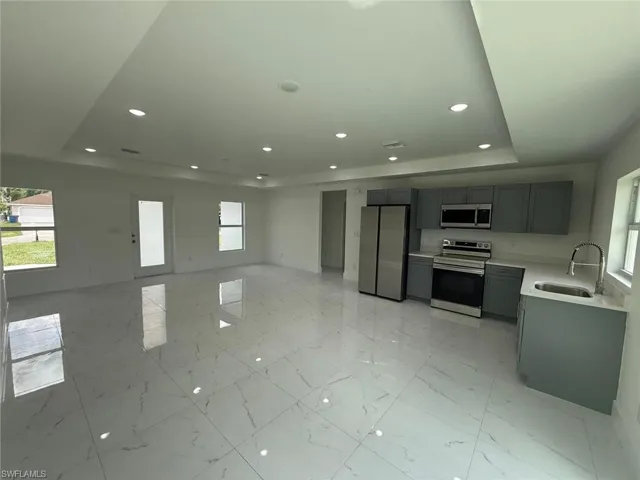 Kitchen featuring a raised ceiling, stainless steel appliances, recessed lighting, gray cabinets, and light marble finish floors