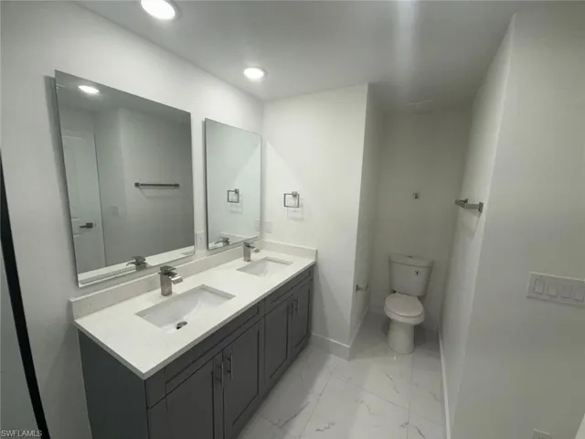 Full bath featuring double vanity and light marble finish flooring