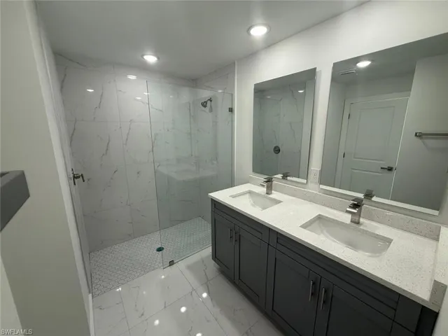 Full bathroom with a marble finish shower, double vanity, light marble finish floors, and recessed lighting
