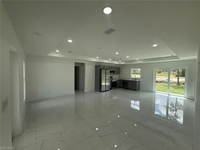 Unfurnished living room featuring a raised ceiling, light marble finish flooring, and recessed lighting