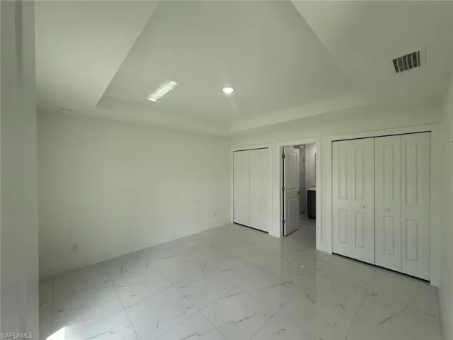 Unfurnished bedroom featuring light marble finish floors, a tray ceiling, multiple closets, and recessed lighting