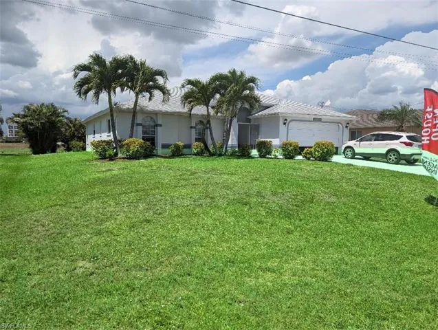 Single-story residence featuring a two-car garage, established front landscaping, palm trees, and a spacious front lawn